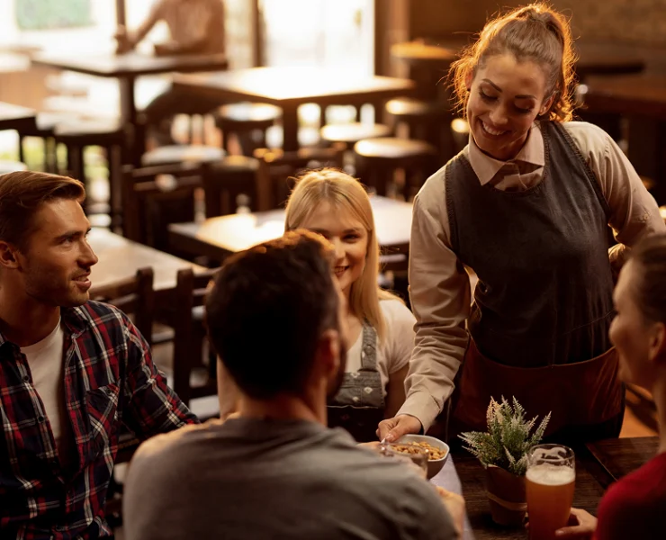 Restaurant server delivers food to four guests seated around a table in a warmly lit dining room.